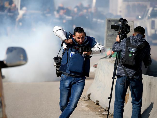 Journalists demonstrate as tear gas are fired by Israeli forces during a march organized by Palestinian and foreign journalists to demand safety measures at the Qalandiya checkpoint, between Jerusalem and Ramallah, in the occupied West Bank on November 17, 2018. (Photo by ABBAS MOMANI / AFP)