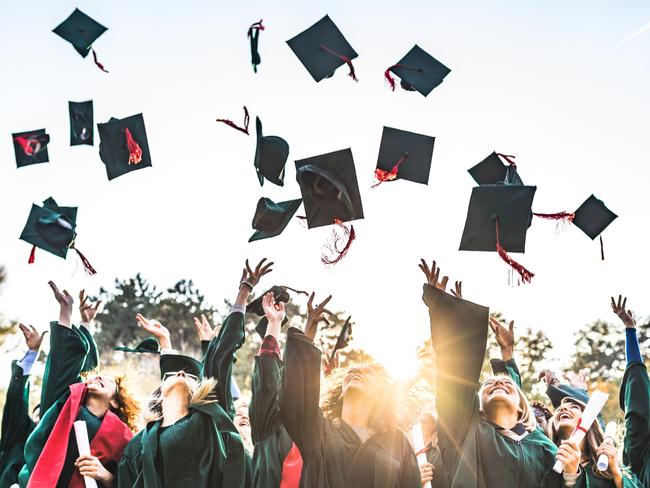 Generic stock photo showing a large group of happy college students celebrating their graduation day outdoors while throwing their caps up in the air.