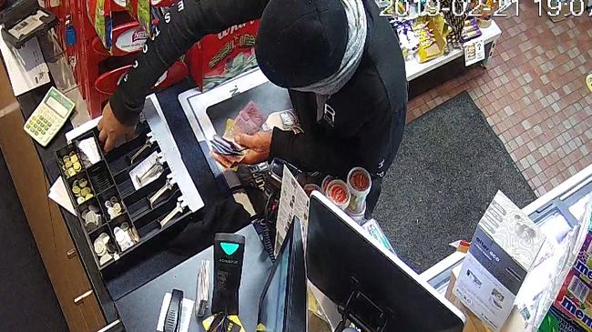 CCTV image of a robber armed with a kitchen knife grabbing cash from the till while holding up the Budget Service Station on Harbord Rd, Freshwater. Source: NSW Police