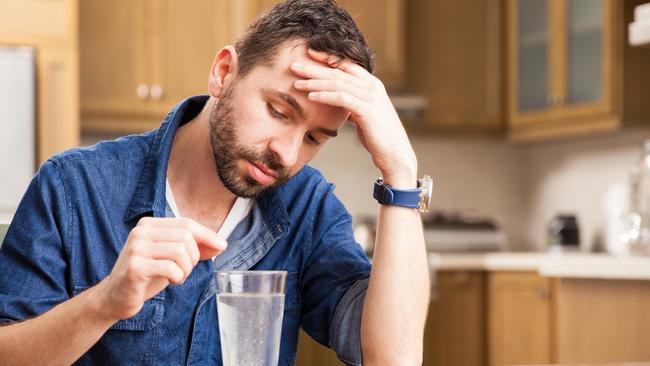 Guy with a beard and a denim shirt waiting for an effervescent tablet to dissolve and cure his indigestion at home