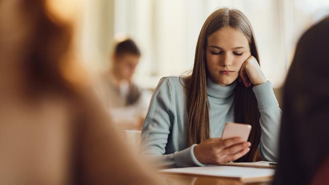 A student uses a mobile phone while feeling bored in a class at high school.