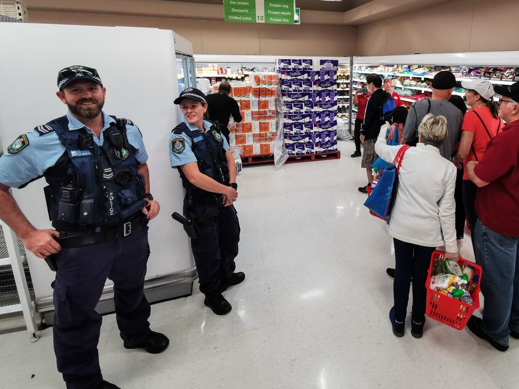 Police watch as people queue for a delivery of toilet paper, paper towel and pasta at Coles Supermarket, Epping, in Sydney on Friday. Picture: AAP Image/James Gourley.