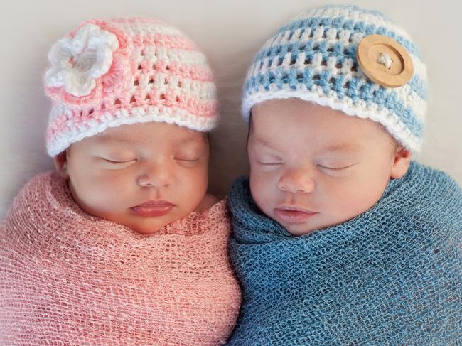 Five week old sleeping boy and girl fraternal twin newborn babies. They are wearing crocheted pink and blue striped hats.