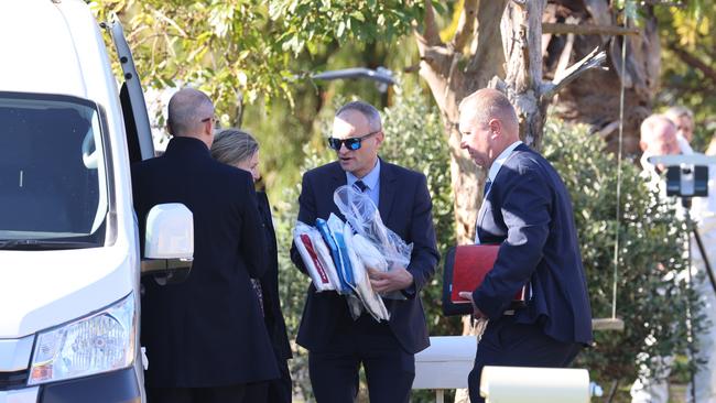 A Detective carries evidence and documents as a police search of the home continues. Picture: Russell Millard