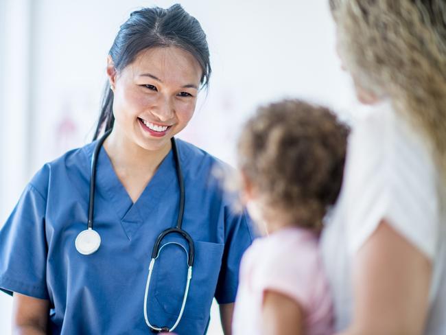 Female doctor with a stethoscope and scrubs in a medical office with a young girl patient and the mother