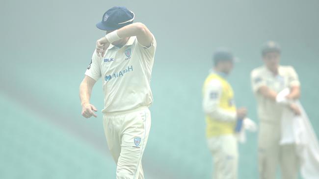 NSW players guard their eyes from smoke haze during a Sheffield Shield game.