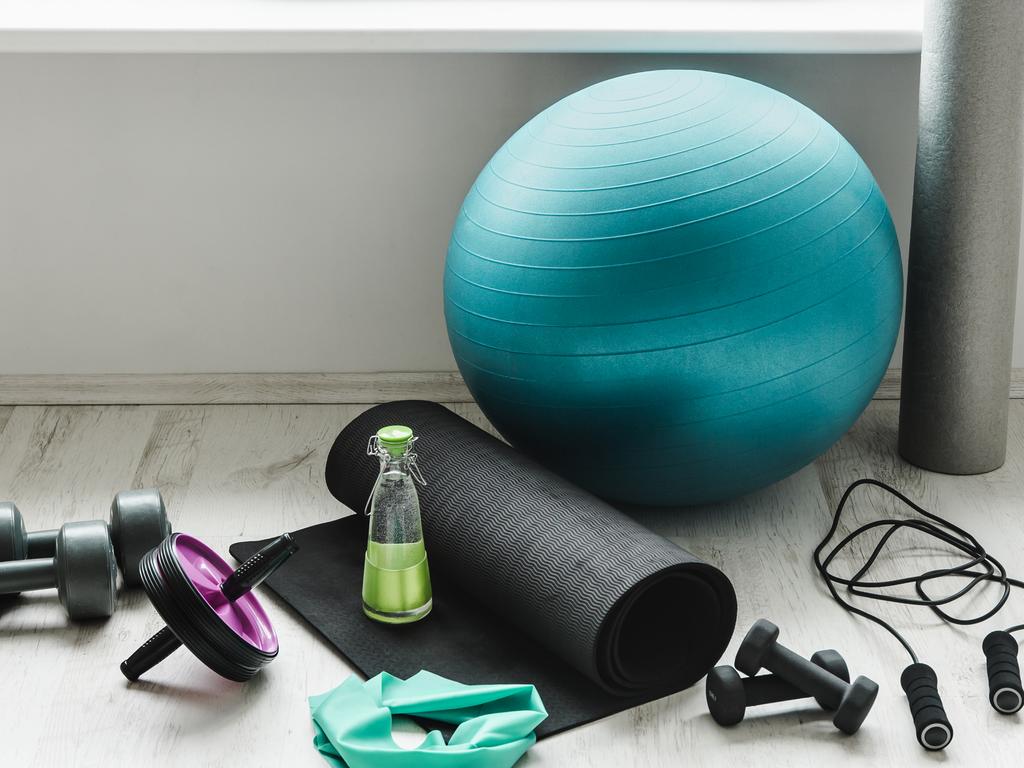 Group of different exercising equipment on white home gym floor. Fitness ball, round foam roller, resistance exercise latex band, jumping rope, dumbbells, yoga mat. Fit lifestyle concept.