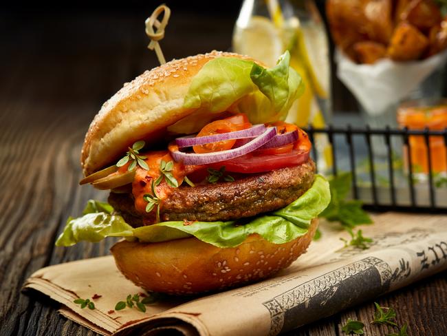 Falafel burger with addition of lettuce, tomato, onion, pickle cucumbers, spicy aromatic sauce and herbs on a wooden rustic table. Vegetarian food tasty and nutritious