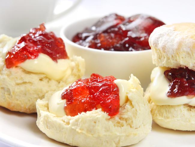 Scones with strawberry jam and clotted cream, served with a cup of tea.