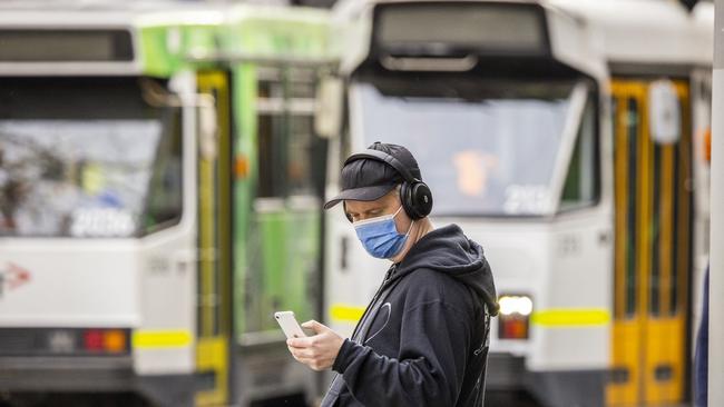 A man looks at his phone in front of Melbourne trams. Picture: NCA NewsWire / Wayne Taylor