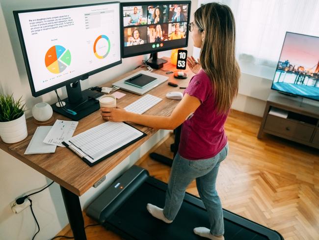 Woman working from home at standing desk is walking on under desk treadmill