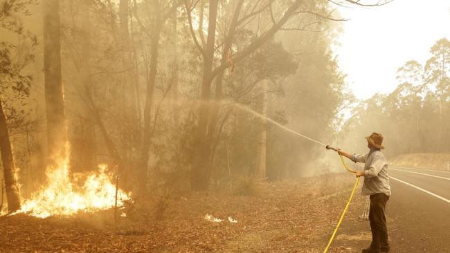 A man uses a water hose to battle a fire near Moruya on the NSW south coast on Saturday. Picture: AP/Rick Rycroft