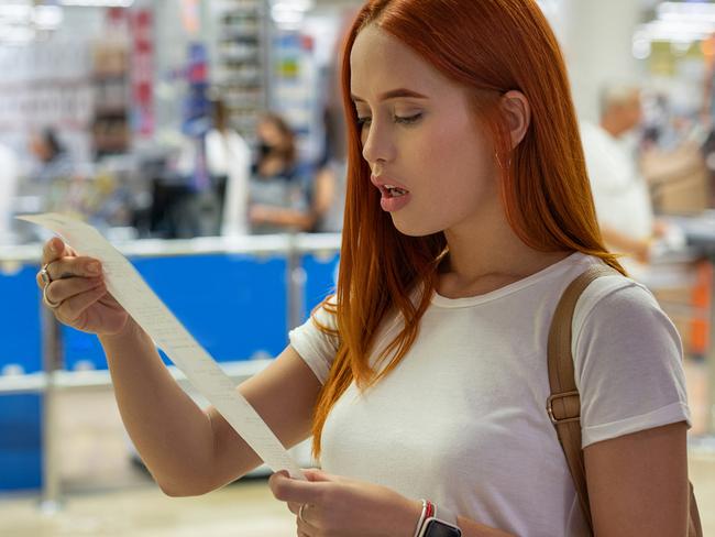 Surprised woman looks at receipt total with food in mall