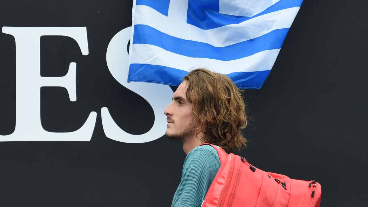 Greece's Stefanos Tsitsipas walks past a Greece national flag.