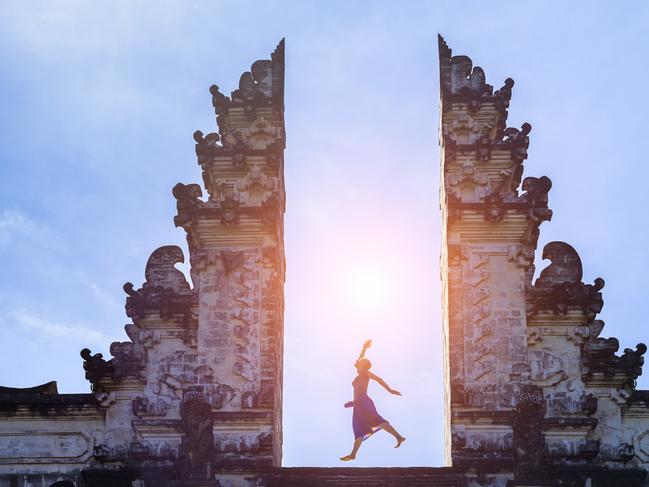 ESCAPE: Woman traveler jumping with energy and vitality in the gate of a temple, Bali, Indonesia. Picture:  Istock