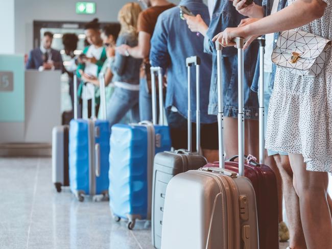 Travelers with luggage using smart phones while waiting in line for boarding at airport. Focus on wheeled luggage.Escape 9 June 2024Doc HolidayPhoto - iStock