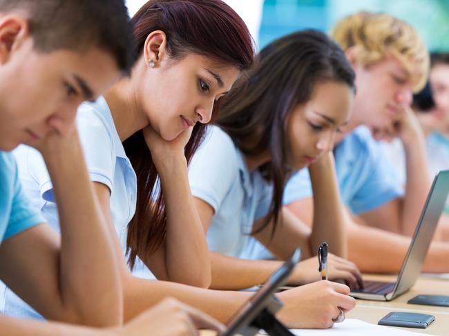 Row of private high school students work on assignment in class. They are writing or using laptops or digital tablets. They are concentrating as they study. They are wearing school uniforms. Picture: iStock