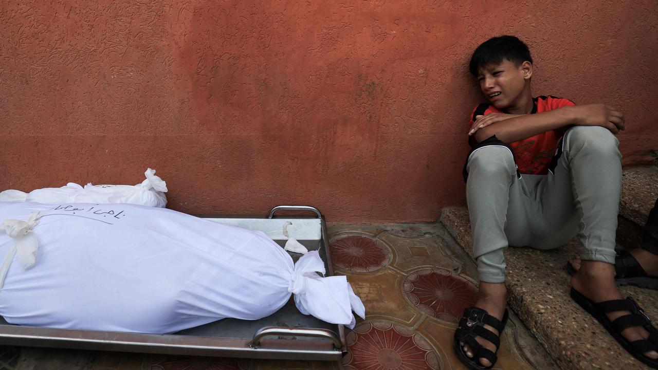 A young boy from the Abu Hamad family reacts in grief a he sits next to the shrouded bodies of his father and two brothers before being collected for burial from the al-Nasser hospital in Khan Yunis in the southern Gaza Strip on November 9, 2023. Picture: Mahmud HAMS / AFP