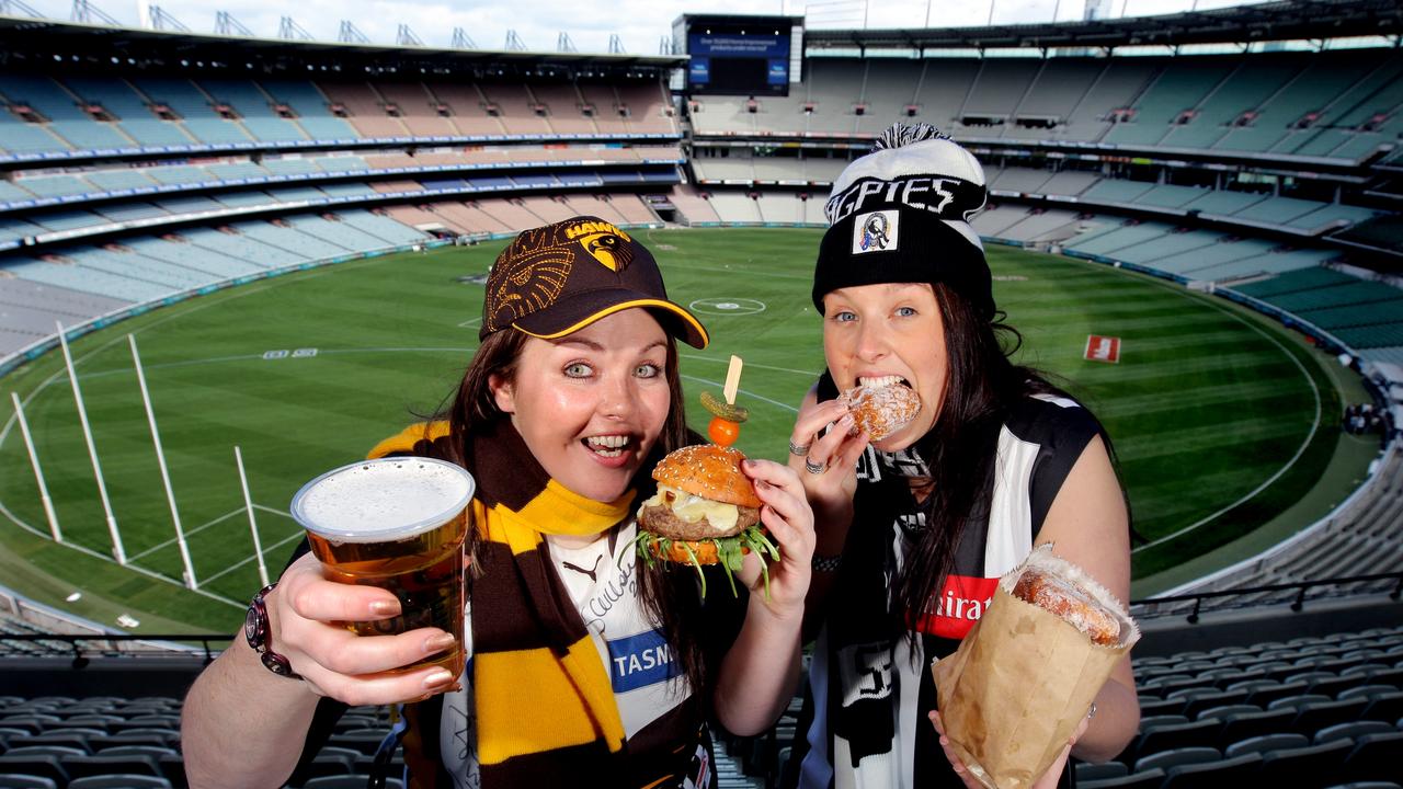 Hawthorn fan Nicole Menzel with a burger and a beer and Collingwood fan Mikelle Stott with a bag of doughnuts at the MCG.