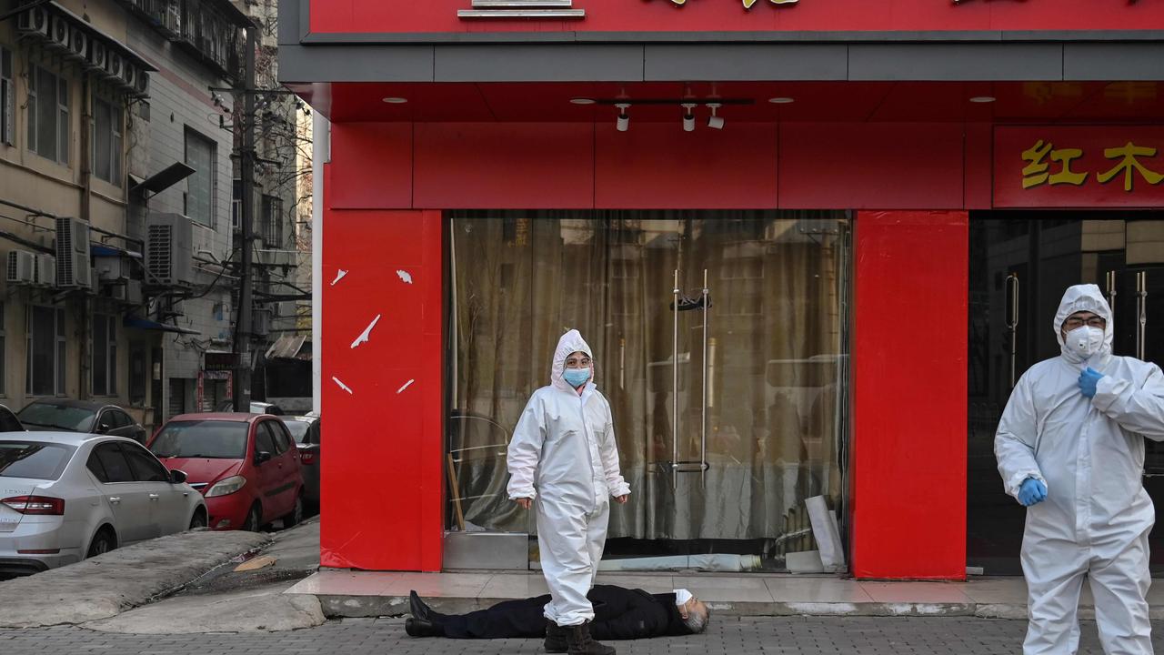 Officials in protective suits checking on an elderly man wearing a face mask who collapsed and died on a street near a hospital in Wuhan. Picture: AFP