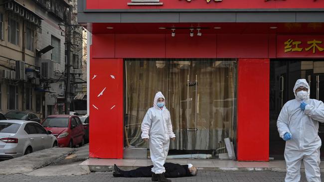 Officials in protective suits checking on an elderly man wearing a face mask who collapsed and died on a street near a hospital in Wuhan. Picture: AFP