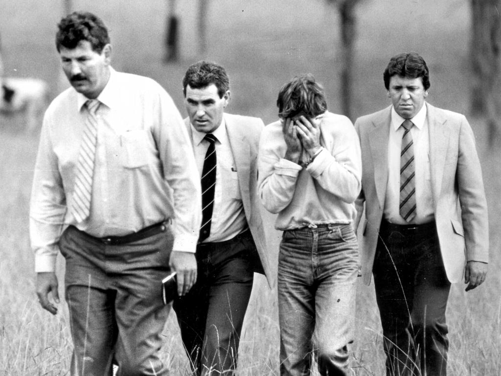 Murphy covers his face as detectives walk the convicted rapist and murderer through the Prospect paddock where Ms Cobby was killed. 