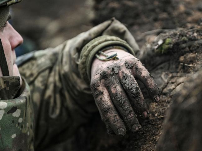 TOPSHOT - A Ukrainian serviceman takes cover in a trench near Bakhmut in the Donbas region on March 8, 2023. - After a cold and snowy winter, the arrival of spring with rain and milder temperatures has brought back the mud on the Donbas battle fields. Trenches that have become baths where soldiers wade through and trucks, armoured cars and sometimes tanks destroyed after getting stuck in mud. (Photo by Aris Messinis / AFP)