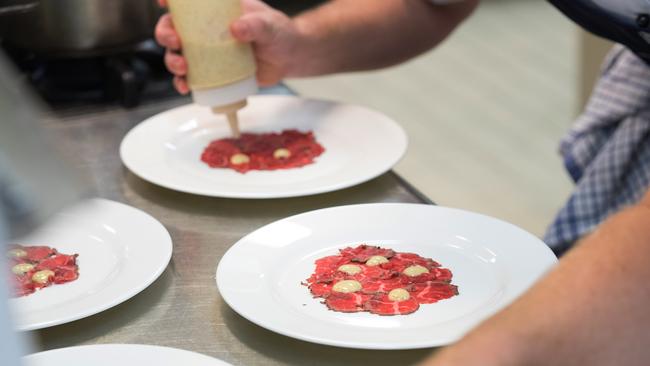 Plating up carpaccio of hanger, pickled beetroot and enoki, crispy kipfler, shallot rings and four pines emulsion