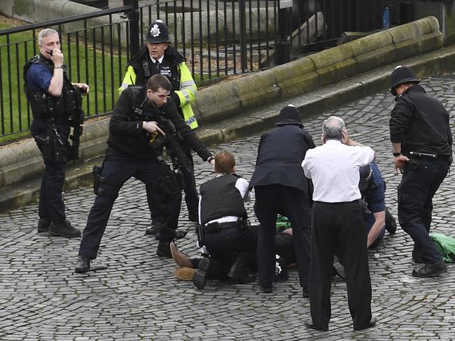 An armed police officer stands over emergency services treating the suspect outside the Palace of Westminster, London. Picture: AP
