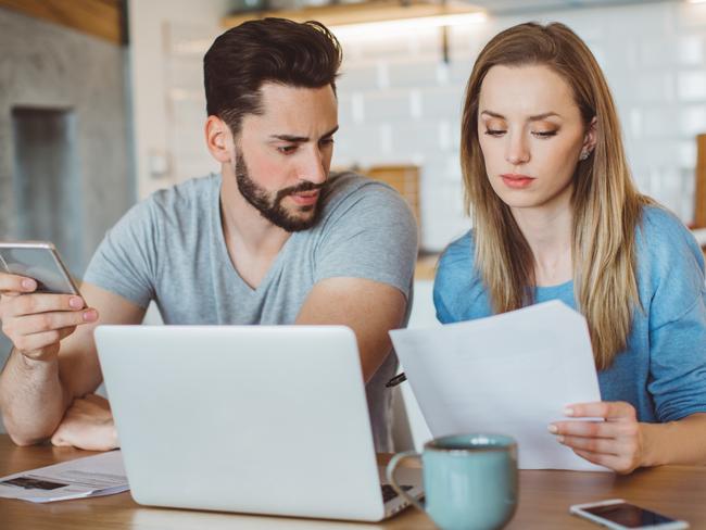 Young couple worried about their finances at home. They are wearing pajamas and drinking first coffee of the day at the kitchen.