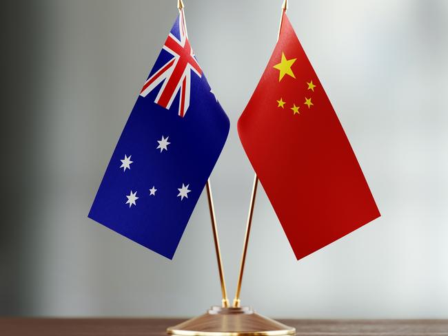 Australian and Chinese flag pair on desk over defocused background. Horizontal composition with copy space and selective focus.