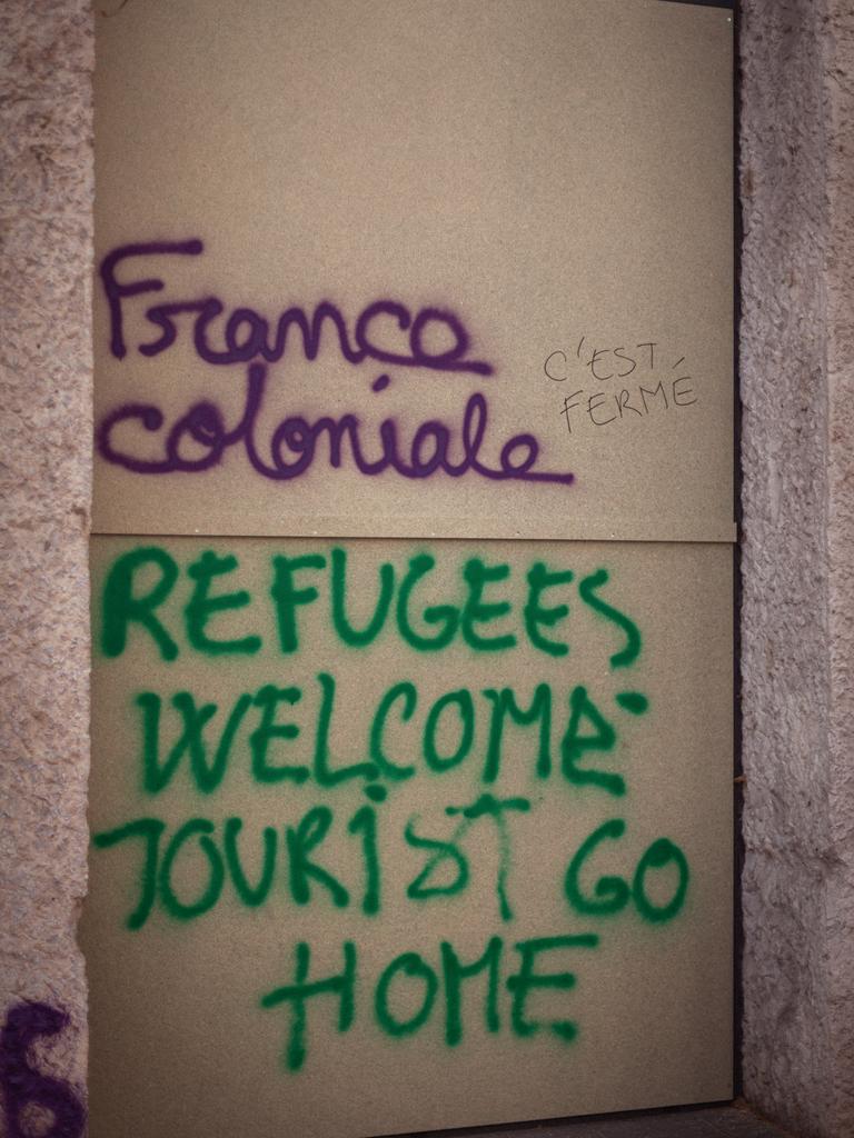 A wall is spray-painted ‘Colonial France’ and ‘Refugees welcome tourists go home’ in Lyon, France. Picture: AFP