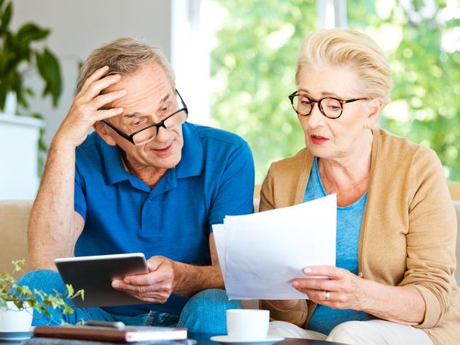 Worried mature woman and man sitting on sofa in living room at home. Senior couple watching bills and calculating monthly expenses.