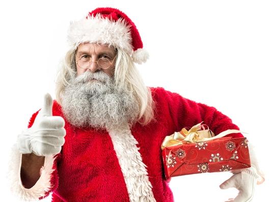 RendezView. Santa Claus holding a gift and signing thumb up with the other hand. He is wearing the traditional clothing with the red cap, jacket and trousers, the black belt and golden glasses. (Pic: iStock)
