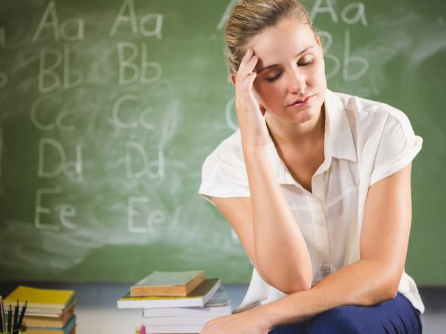 Tensed school teacher sitting with hand on forehead in classroom at school