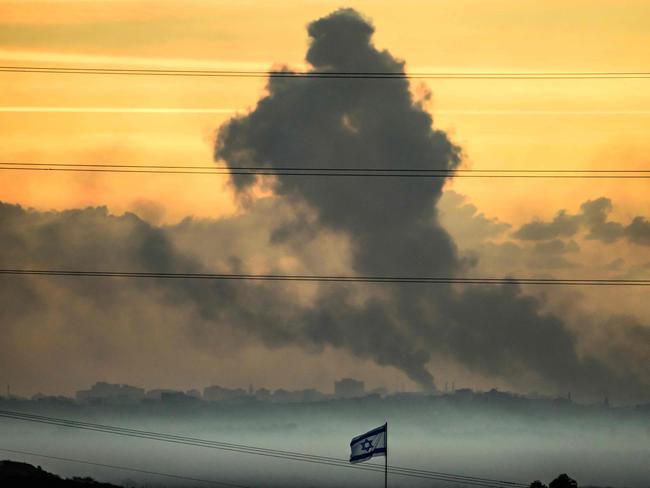 This picture taken from a position in southern Israel near the border with the Gaza Strip shows an Israeli flag waving as smoke billows in the Palestinian territory after an Israeli strike. Picture: AFP