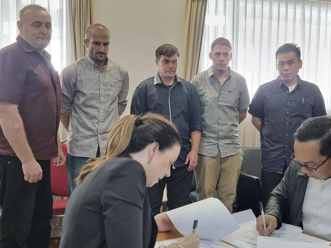 In this photo released by the Indonesian Coordinating Ministry for Legal, Human Rights, Immigration and Correctional Affairs, Indonesian and Australian officials sign handover documents as five Australians who have spent almost 20 years in Indonesian prisons for heroin trafficking look on, prior to their return to Australia, in Bali, Indonesia, Sunday, Dec. 15, 2024. (Indonesian Coordinating Ministry for Legal, Human Rights, Immigration and Correctional Affairs via AP)