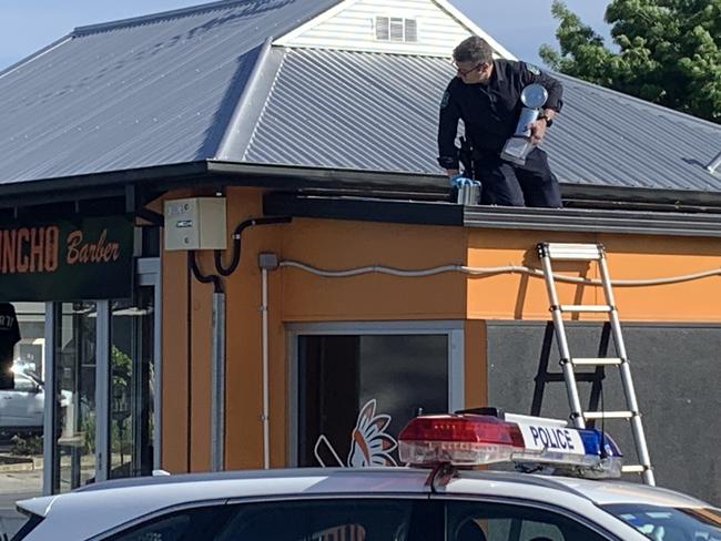 Crime scene investigators pictured on the roof examining a crawl space above the barber shop. Picture: George Yankovich