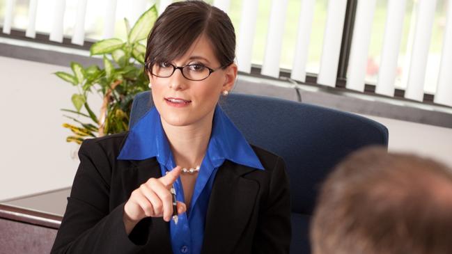 CAREERS: Color stock photo of a young businesswoman sitting in an office at a desk lecturing or questioning a young businessman.