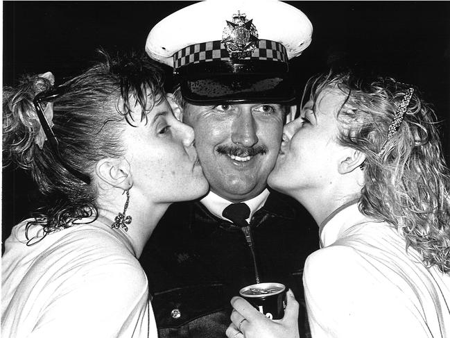 In 1987 Sergeant Mike Andrews gets a new years’ kiss from 19 year-olds Kristen Potts and Bronwyn Goucher at Barwon Heads. Picture: Bruce Long