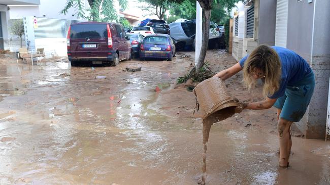 A resident cleans her house next to cars piles due to mudslide in a flooded area in Paiporta, near Valencia, eastern Spain, on October 30, 2024. (Photo by Jose Jordan / AFP)