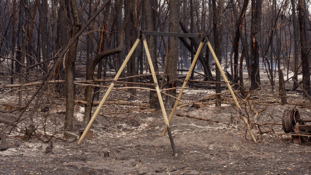 A child's swing sits blackened under burnt bushland, the seat lost to the flames.