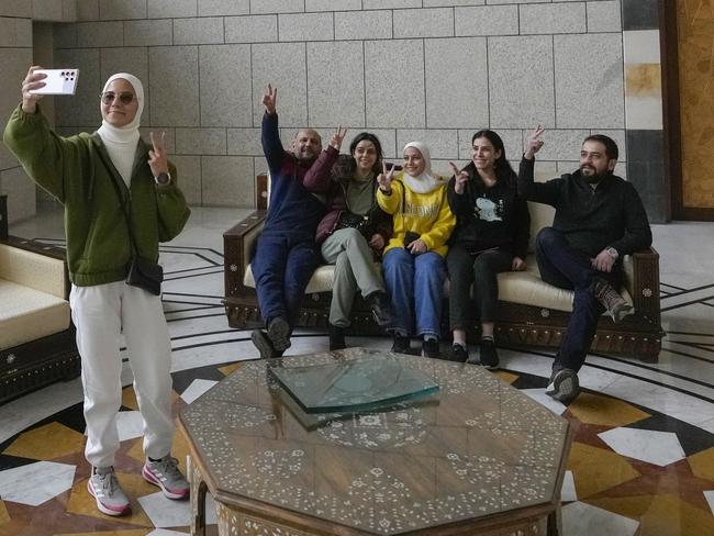 A group of people take a family photo while sitting on a couch in a hall of Syrian President Bashar Assad's presidential palace in Damascus, Syria, Sunday, Dec. 8, 2024. (AP Photo/Hussein Malla)