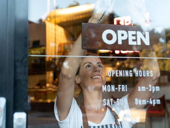 Portrait of a happy business owner hanging an open sign on the door at a cafe and smiling - food and drinks concepts