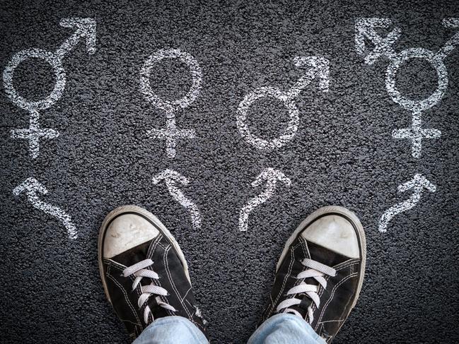 A person standing on asphalt road with gender symbols of male, female, bigender and transgender.  Concept of choice or gender confusion or dysphoria. Istock