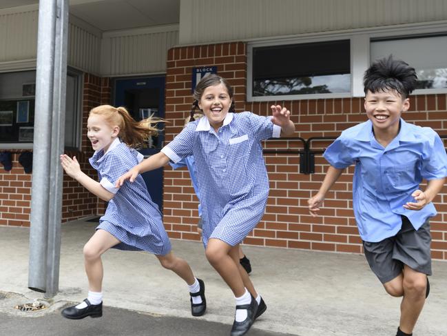 Excited children outside school wearing blue uniforms and smiling