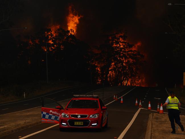 A New South Wales Police officer prepares to flee his roadblock on the Princes Highway near the town of Sussex Inlet on December 31, 2019 in Sydney, Australia. More than 1500 firefighters are currently battling more than 100 blazes across the NSW, with more than 30 fires still yet to be contained. There had been calls for the Sydney New Year's Eve fireworks display to be cancelled due to the ongoing bushfires in NSW, however event organisers have decided to continue as planned following approval from commissioner of the NSW Rural Fire Service Shane Fitzsimmons. Picture: Sam Mooy/Getty