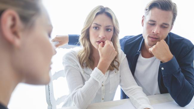 Real estate agent with couple looking through documents. The agent is holding a digital tablet showing it to the clients. Couple are casually dressed. first home buyer generic sad, stressed