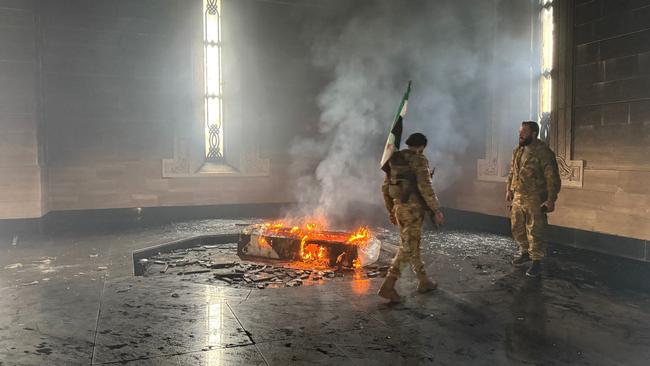 Rebel fighters stand next to the burning gravesite of Syria's late president Hafez al-Assad at his mausoleum in the family's ancestral village of Qardaha. Picture: Aaref Watad / AFP