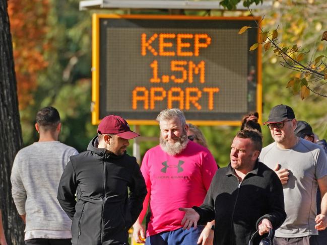 People walk along the Tan Track near a sign with a message to help slow the spread of the coronavirus (COVID-19) disease in Melbourne, Sunday, May 24, 2020.  Under an easing of coronavirus restrictions, Victorians will be allowed to have up to 20 people in their homes and stay overnight at tourist accommodation from June 1.  (AAP Image/Scott Barbour) NO ARCHIVIN2